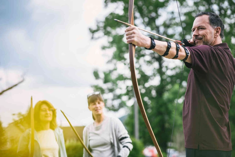Mann spannt einen Bogen in der Natur, neben ihm andere Menschen
